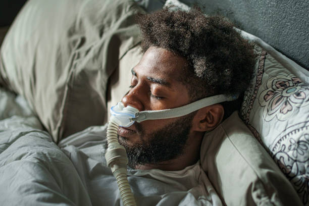 istock Athletic Young African American Man in His Twenties Sleeping Peacefully Using a CPAP Machine (contenuous positive air pressure) in a Dark Bedroom 2204039290