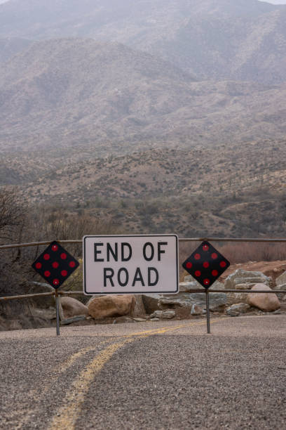 End of road sign on highway below desert mountains