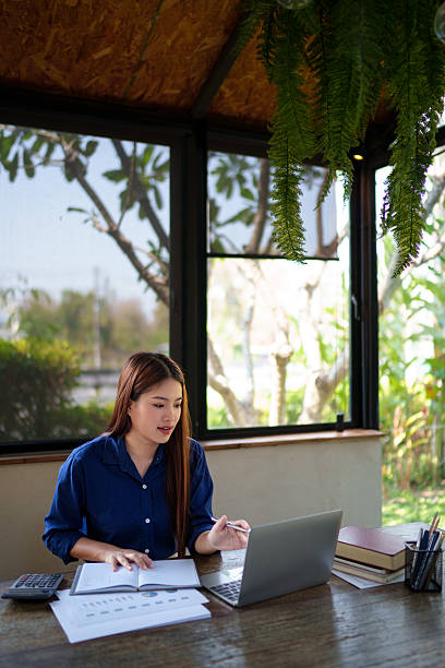 istock Businesswoman calculating company budget using a calculator and documents at a natural-themed workspace with a laptop. 2204064581