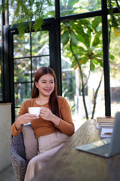 istock Businesswoman holding a coffee cup in a natural-themed office, taking a break from work, relaxing and thoughtful moment. 2204064650