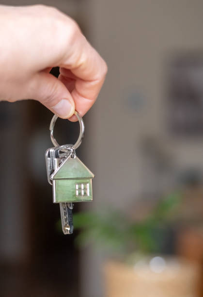 istock Hand holding house keys with a small house shaped keychain, symbolizing the purchase or ownership of a new property, investment, or mortgage 2204074097