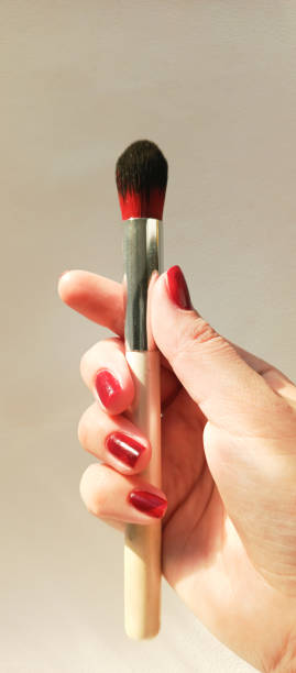 istock A makeup brush in a woman's hand in sunlight on a white background. Makeup. Eye shadow brush. Brush pile. 2204074801