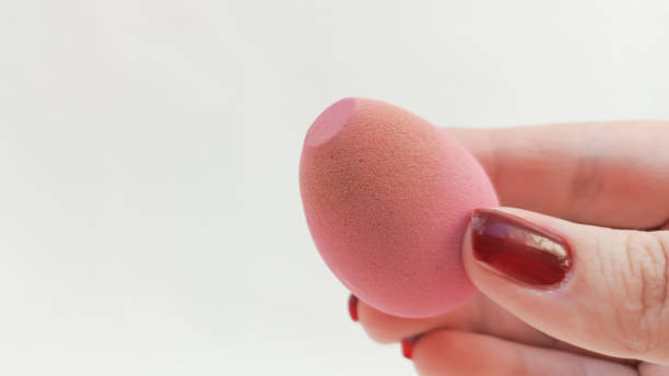 istock A pink sponge stained with foundation in a woman's hand on a white background, a place for text. Applying foundation to the skin 2204074916