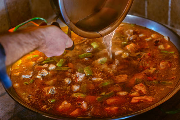 Chef pouring hot water into a paella pan while cooking Valencian paella with the first ingredients.