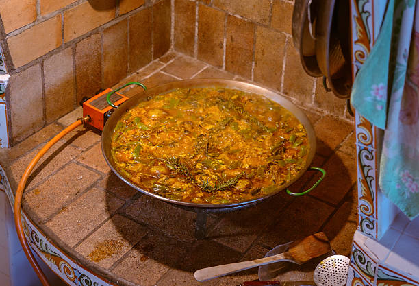 Traditional Valencian paella being cooked in a rustic kitchen on a gas paella pan.