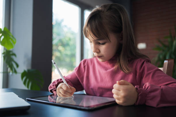 istock Child girl watching online tutorial on laptop computer and drawing digital pictures using digitized pen and digital tablet 2204084641