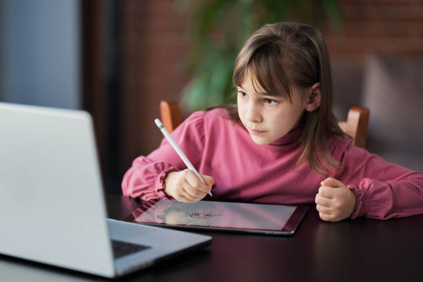 istock Child girl watching online tutorial on laptop computer and drawing digital pictures using digitized pen and digital tablet 2204085027