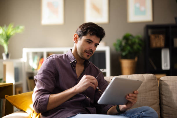 istock Young man chilling on the sofa, focused on his tablet screen 2204099423