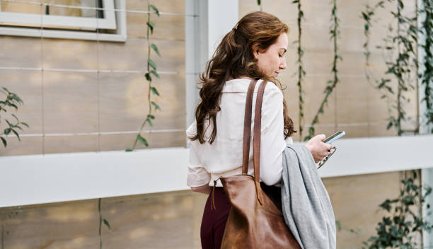 istock Young woman texting on her cell phone while walking outdoors 2204101072
