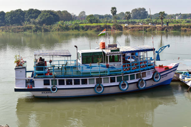 Lalbag, West Bengal, India  January 19, 2025: The image shows a traditional riverboat on the calm Ganges River, surrounded by greenery. The white and blue boat has a covered deck and an Indian flag, depicting charming river transport in India.