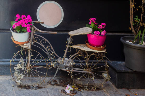 A decorative vintage-style iron bicycle planter adorned with colorful pink flowers in pots, set against a dark urban wall, symbolizing creativity and cheerfulness. Ideal as inspiration for decor and gardening themes.