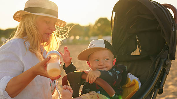 Mother Lovingly Feeds her Child with a Milk Bottle as the Warm Glow of Sunset Surrounds them,The Child Smiles Contentedly,Enjoying the Moment of Care and Comfort