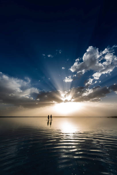 Silhouetted lovers strolling on water with a breathtaking sunrise backdrop. unknown persons