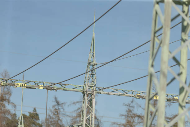 A collection of overhead power lines spans across a vast blue sky, connecting various points in the landscape below, creating an electrical network
