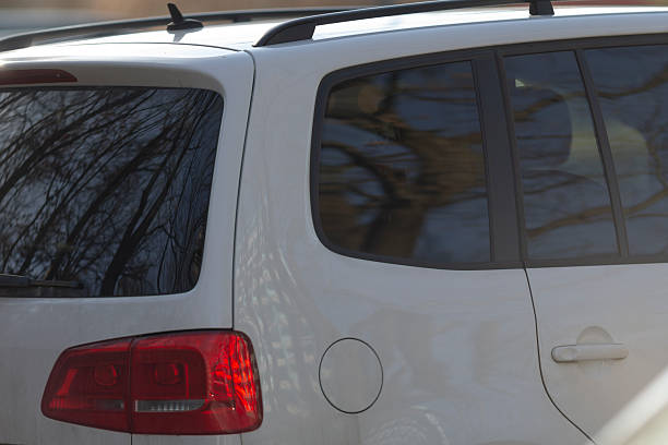 A white SUV featuring a red tail light is currently parked on the side of the road, making it quite noticeable to passersby
