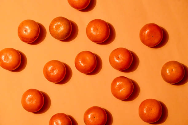 istock Tangerines arranged on an orange background with dramatic shadows – food pattern concept 2204133949