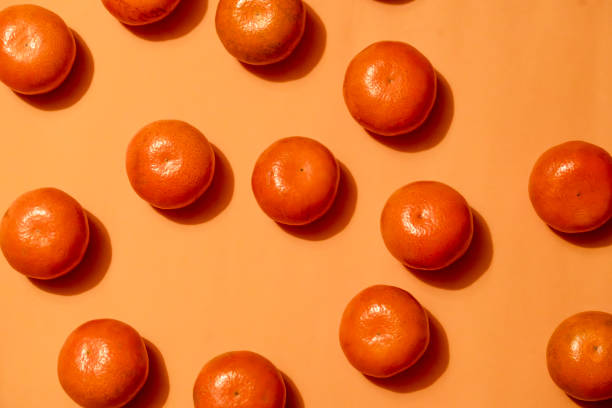 istock Tangerines arranged on an orange background with dramatic shadows – food pattern concept 2204134746