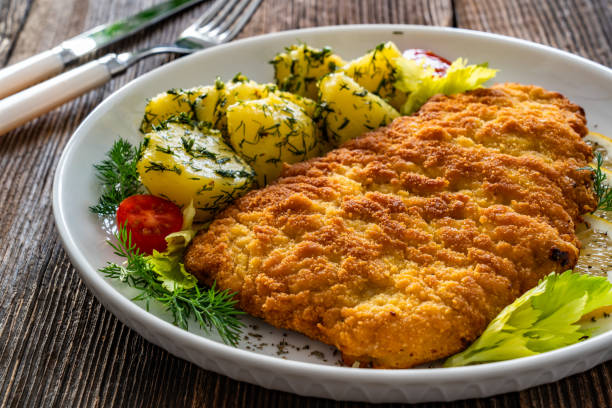 istock Crispy breaded fried pork chop, boiled potatoes and fresh vegetables served on wooden table 2204149728