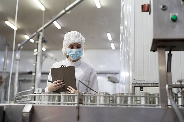 istock Canned fish factory, seafood manufacturing and processing. Food processing. Conveyor belt and workers. Worker in protective gear wearing hairnet inspecting quality of seafood processing conveyor belts 2204151690