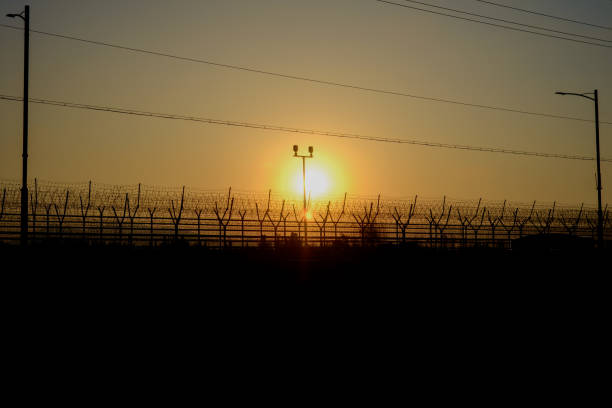 The morning sun rising above the tall barbed wire.