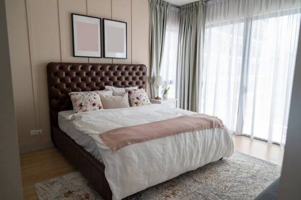 istock Simple modern design with an offer. A double bed with white pillows and a soft blanket, a lamp, and furniture on a wooden floor 2204162400