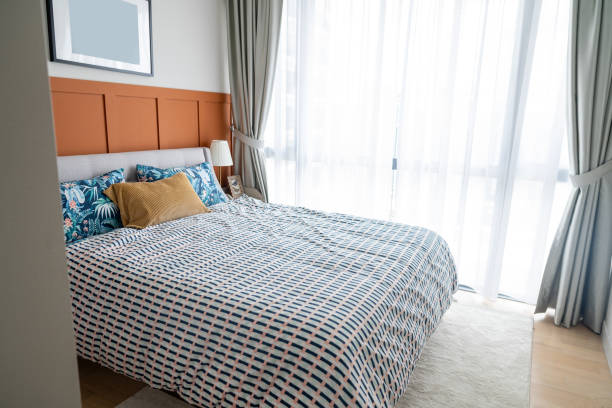 Simple modern design with an offer. A double bed with white pillows and a soft blanket, a lamp, and furniture on a wooden floor.
