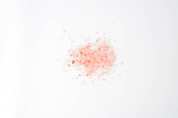 Pink colored Himalayan coarse salt (halite) scattered on the table. Isolated on white background.