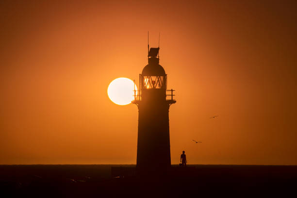 istock Lighthouse at sunset with figure silhouette against orange sky 2204171201
