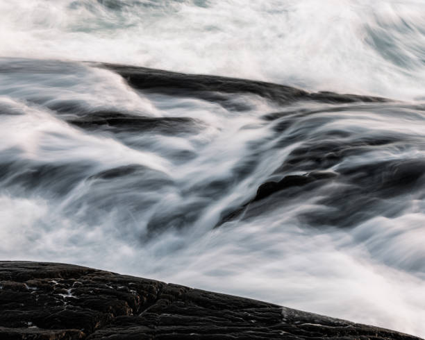 Sweden coastal scenery features dynamic waves crashing against dark rocks at sunset, showcasing natural beauty and tranquility