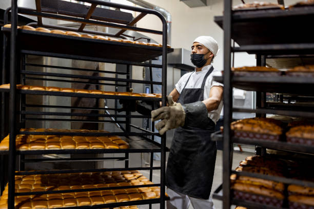 istock Baker moving trays of bread at an industrial bakery 2204192539