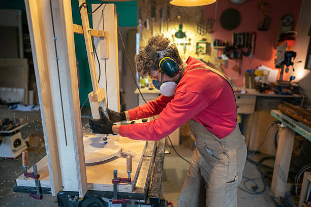 istock Carpenter in protective gear sands stool foundation in wood workshop. Smooth finishing, sculpting 2204195453