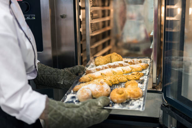 Female baker in uniform taking fresh breads out from oven