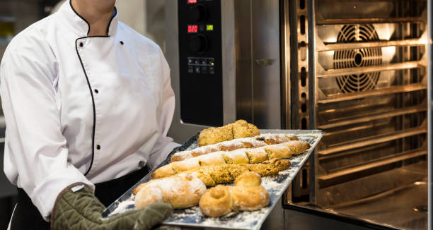 istock Female baker in uniform taking fresh breads out from oven 2204196099