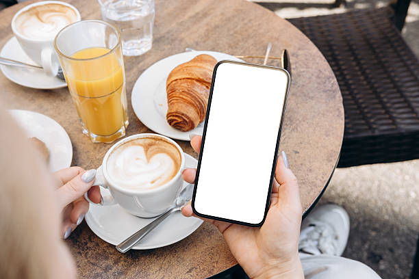istock Mockup woman's hand holding using smart phone with white blank screen POV at cafe on breakfast table, mobile app design and advertising, online marketing 2204197031