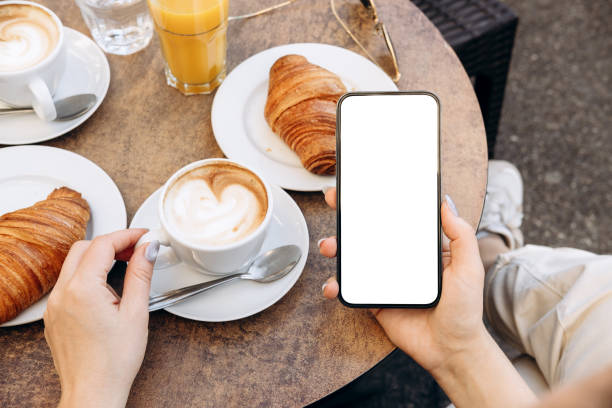 istock Mockup woman's hand holding using smart phone with white blank screen POV at cafe on breakfast table, mobile app design and advertising, online marketing 2204197325