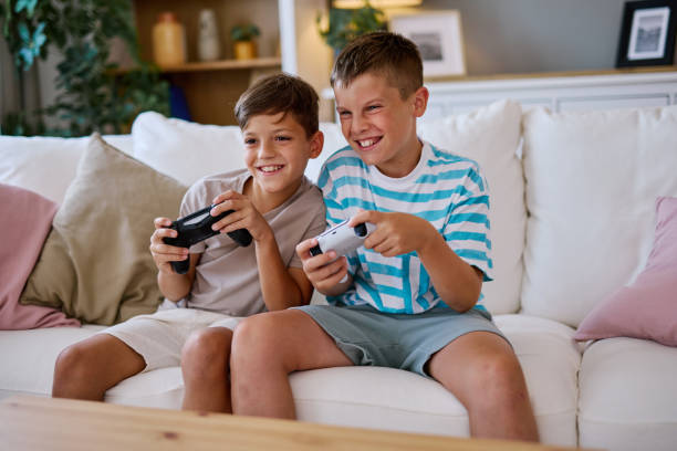 istock Two Brothers playing video games at home sitting on a white sofa 2204197607