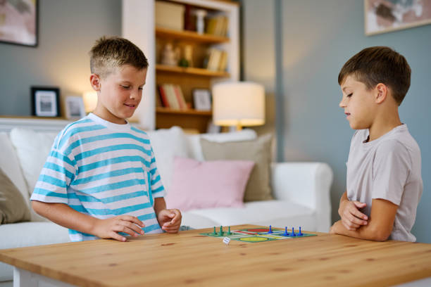 Two brothers sitting at a wooden table in their living room, enjoying a board game together, sharing laughter and developing important skills while having fun and bonding