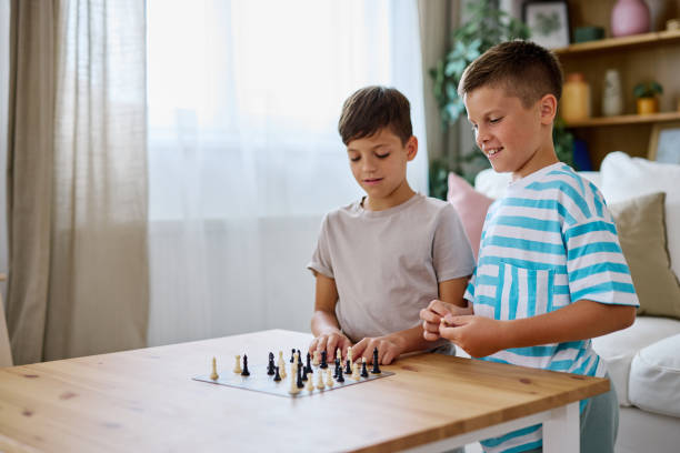 Two young brothers concentrating on a chess game, enjoying quality time together in the living room on a bright, sunny day, sharing laughter and engaging in friendly competition