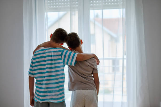 istock Two brothers hugging and looking out the window at home 2204197688