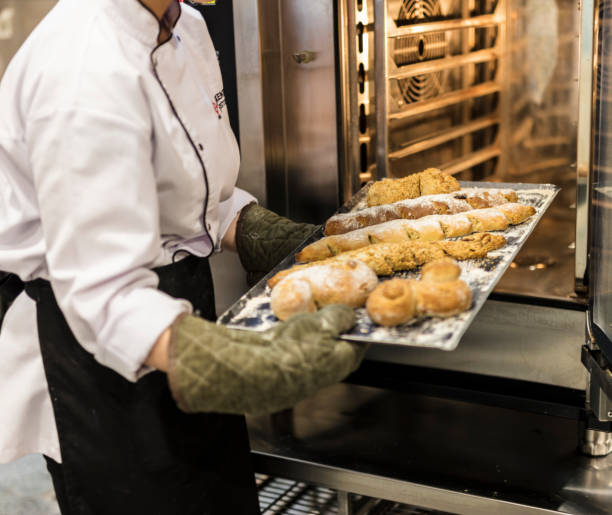 istock Female baker in uniform taking fresh breads out from oven 2204198332