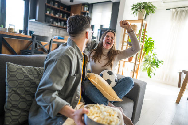 istock Excited couple cheering while watching soccer game on tv at home 2204198582