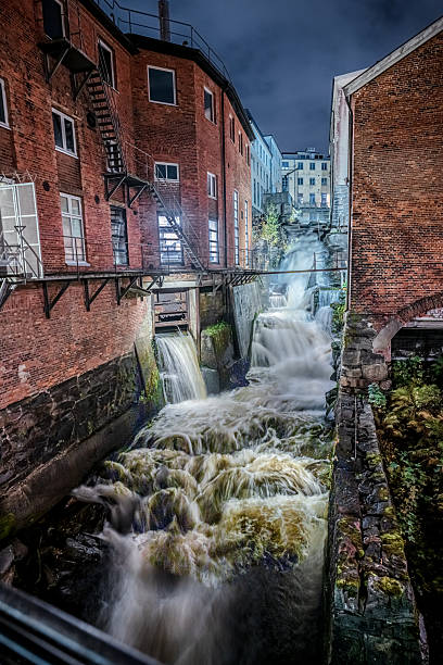 istock rushing waterfall through historic brick industrial buildings at night.. 2204199715
