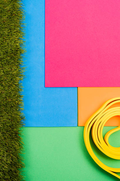 Overhead yellow resistance band lying on multicolored paper backdrop with green, orange, blue, pink hues and artificial grass edging