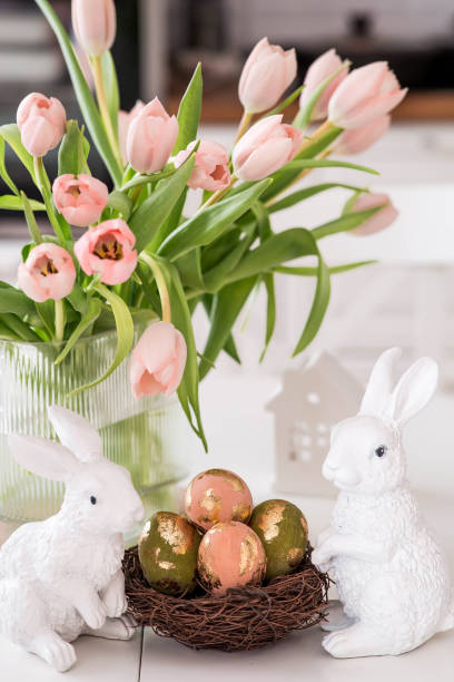 istock A bouquet of delicate tulips, Easter bunnies and eggs with a golden pattern on the table. There is a white kitchen in the background. Beautiful greeting card. The concept of minimalism. 2204203914