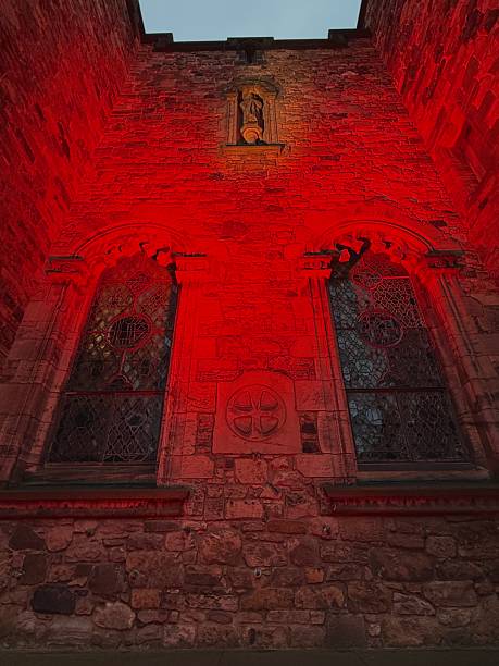 A medieval stone church facade bathed in eerie red light, featuring intricate stained glass windows and a carved statue above.