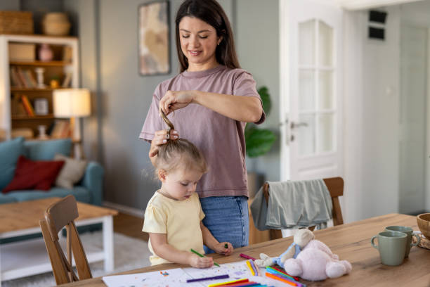 istock Mother tying daughter's hair while she is drawing at home 2204213609