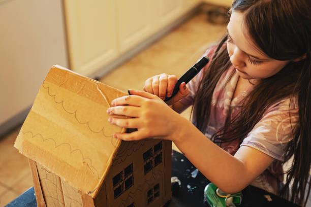 A girl decorates a cardboard home with markers.