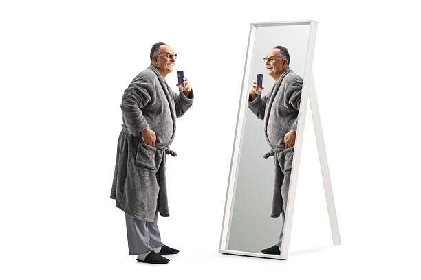 istock Mature man in a bathrobe spraying a perfume in front of a mirror 2204215991