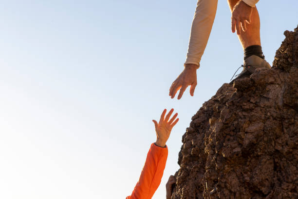 Hiker offers a helping hand in desert at sunset Detail of hiker offering a helping hand to partner on rock summit in desert at sunset, distant mountains and cacti, Apache Junction, Lost Dutchman State Park, Arizona reach destination stock pictures, royalty-free photos & images
