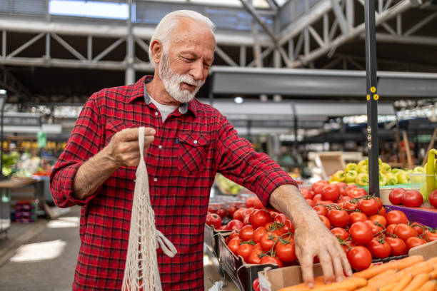istock Senior man choosing tomatoes at farmers market using reusable bag 2204221250